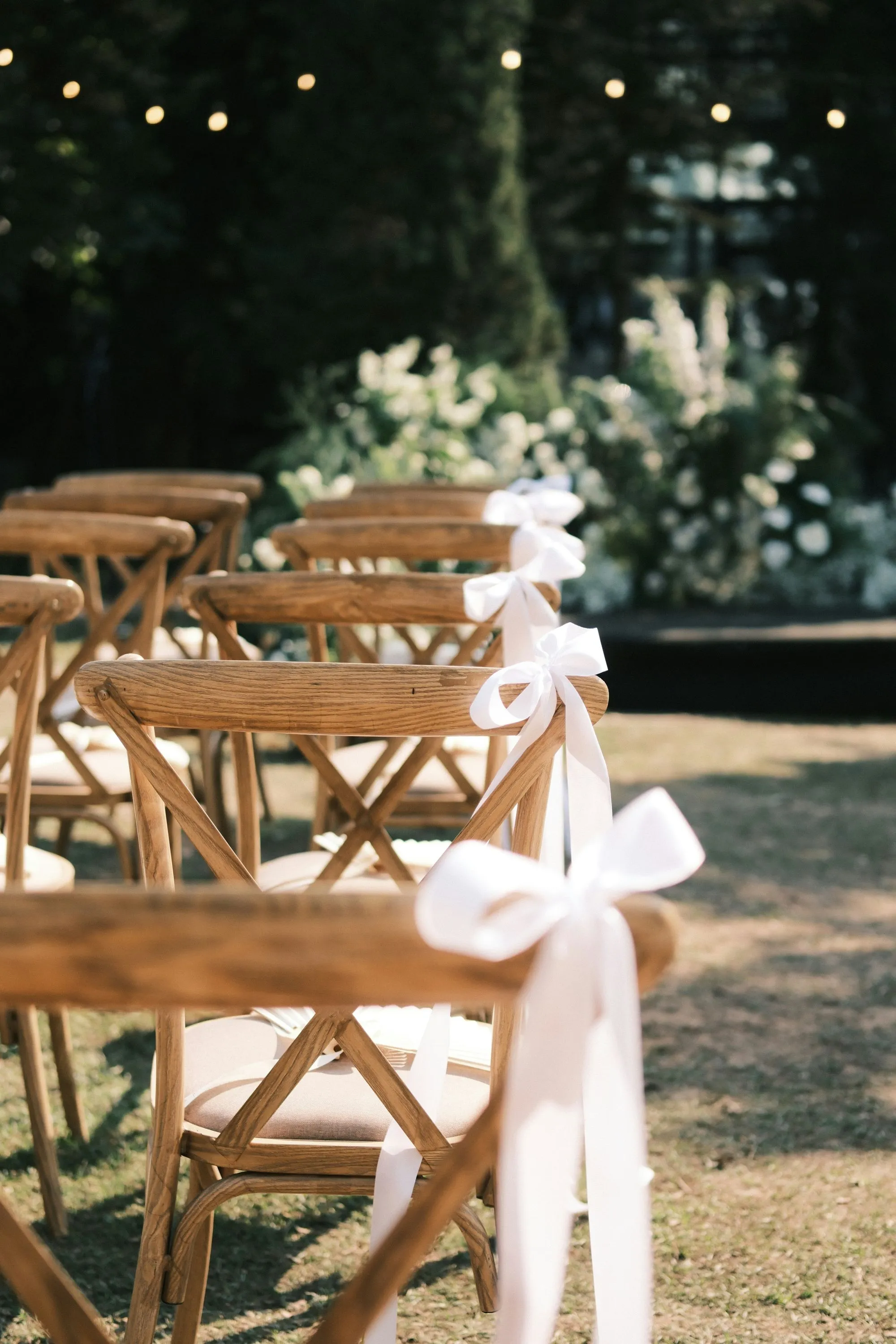 Chaises en bois décorées de nœuds blancs, prêtes à accueillir les invités dans un décor charmant et romantique.