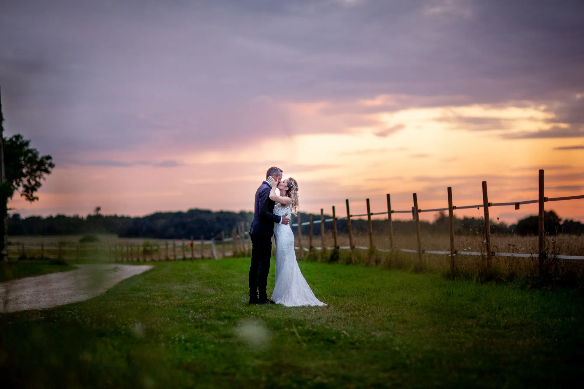 Un couple de mariée et de marié partageant un moment tendre au coucher de soleil, avec un décor paisible de champs et