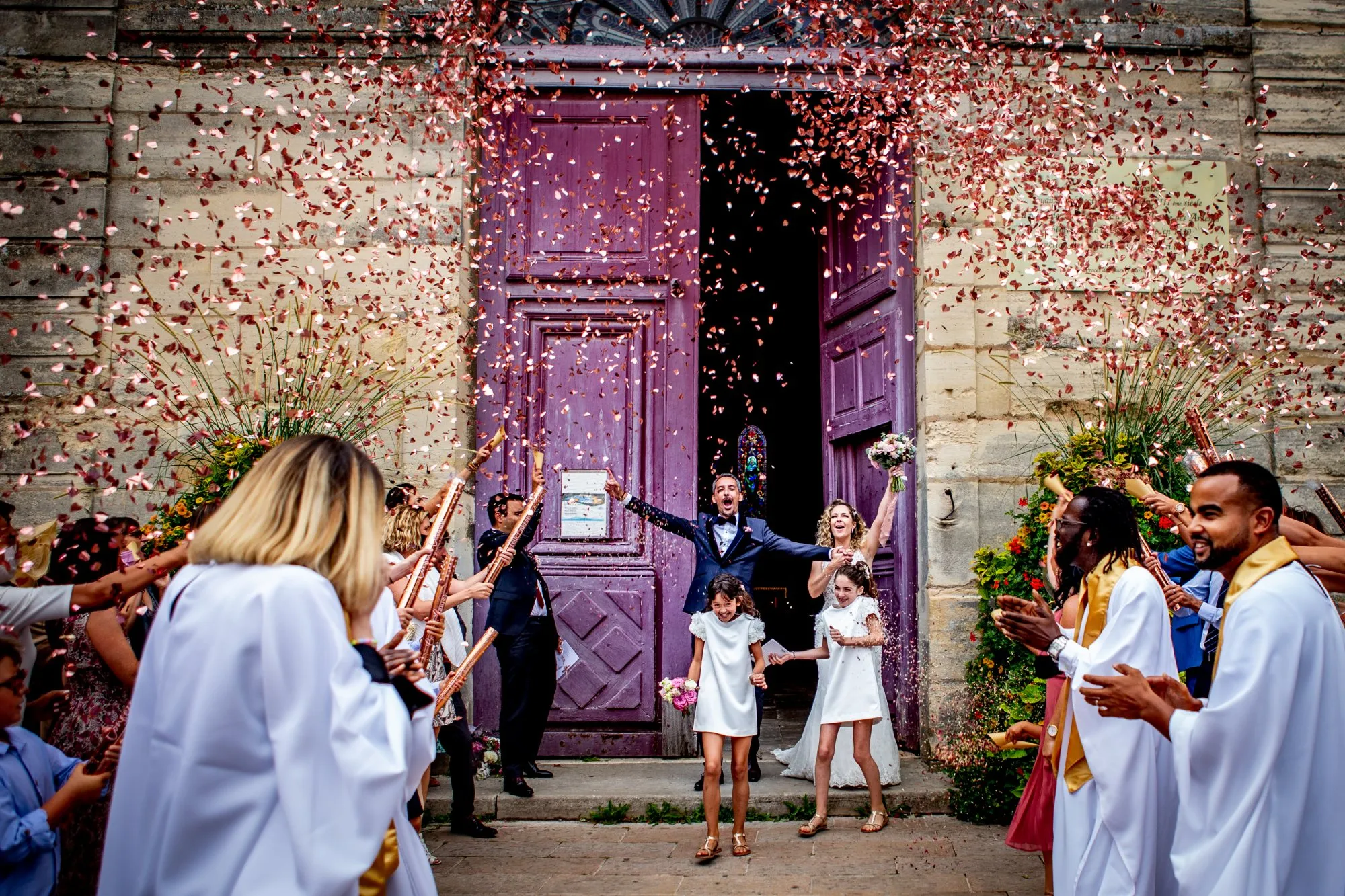 Un couple heureux sort d'une porte violette, entouré de fêtes et de confetti rose, avec des musiciens jouant de la