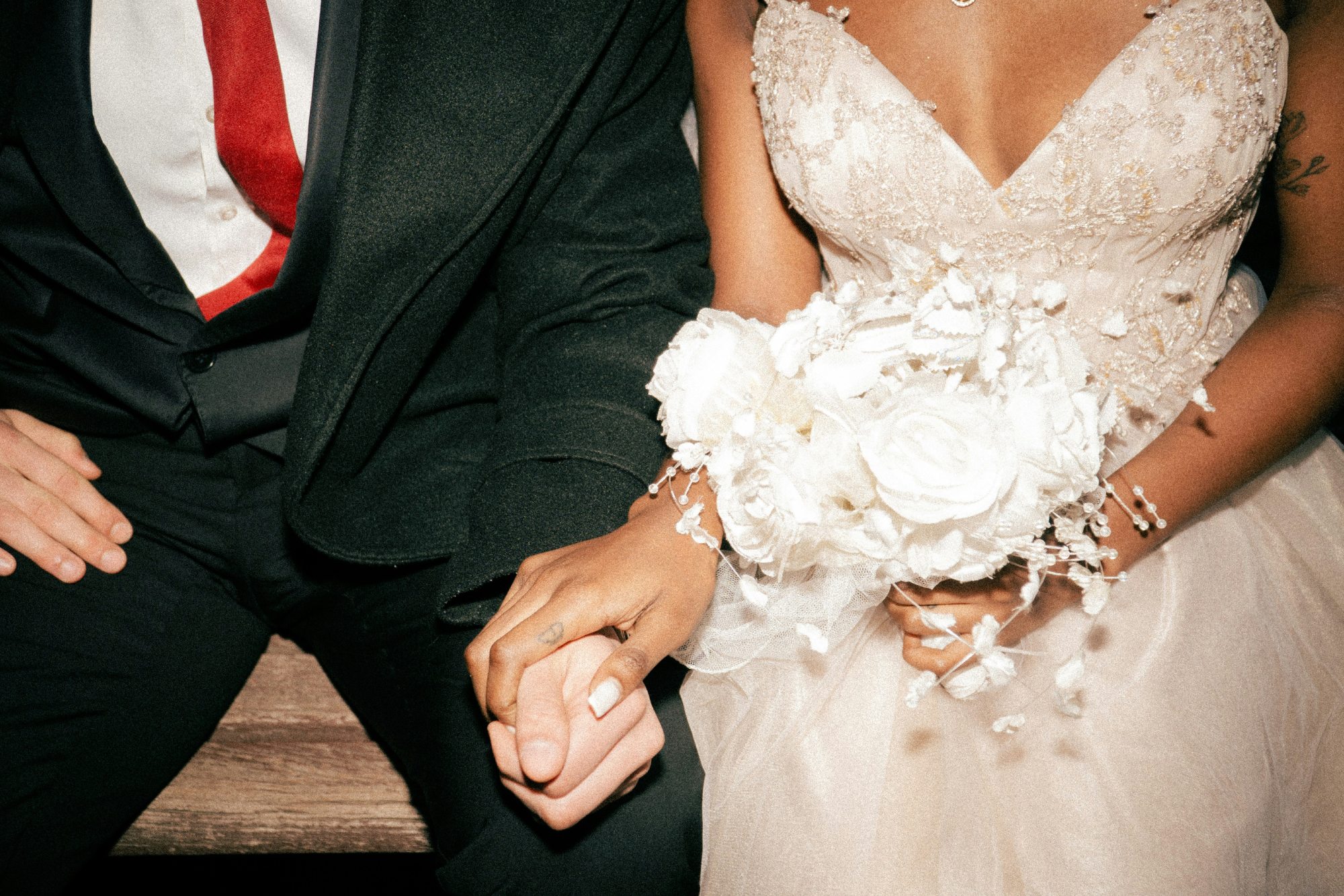 Une mariée en robe blanche et un mari en costume sombre tenant fermement leur main, avec un bouquet de fleurs blanches