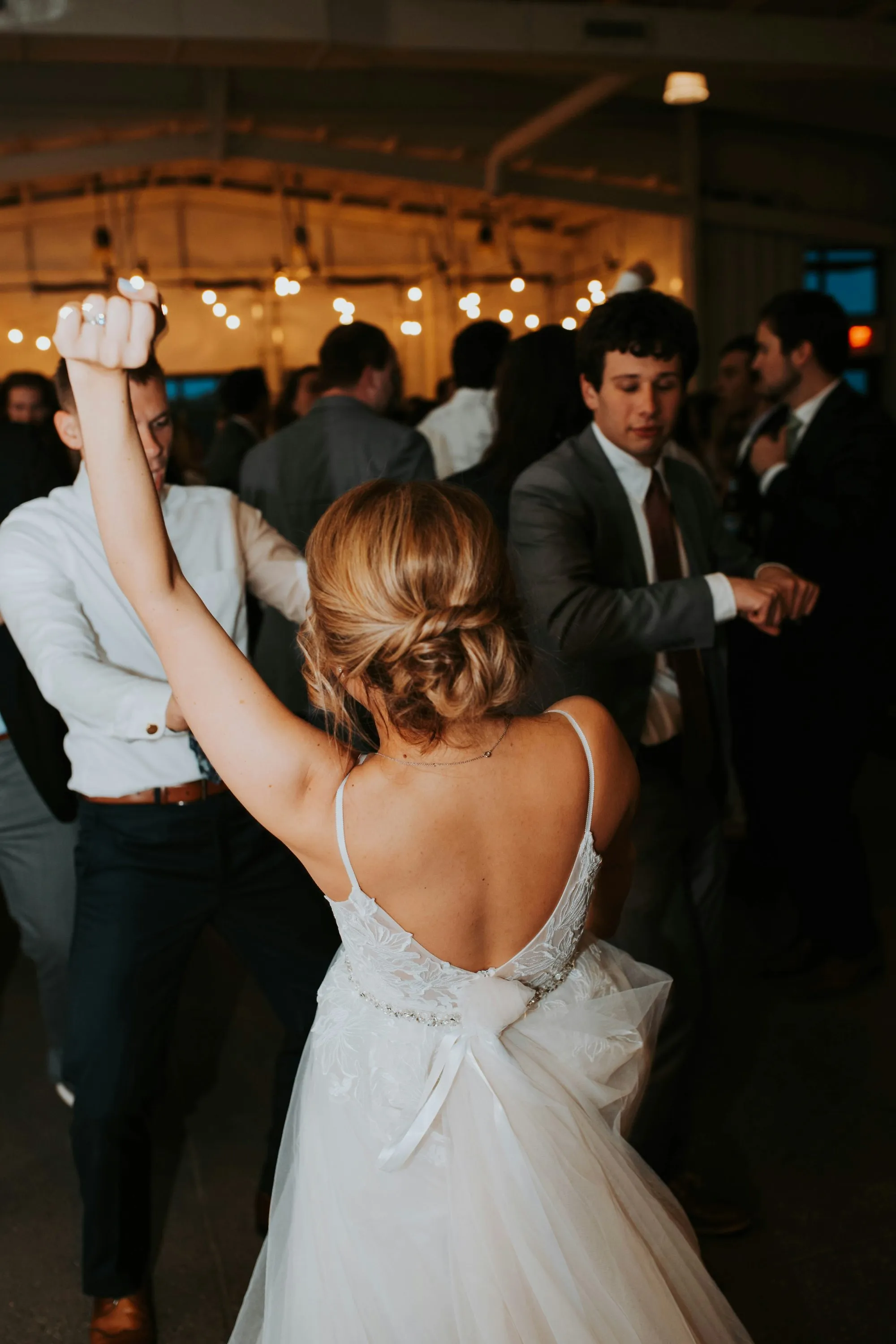 Une mariée dans un robe blanche élégante danse avec un homme en costume, leur main levée dans une ambiance animée et lumineuse.