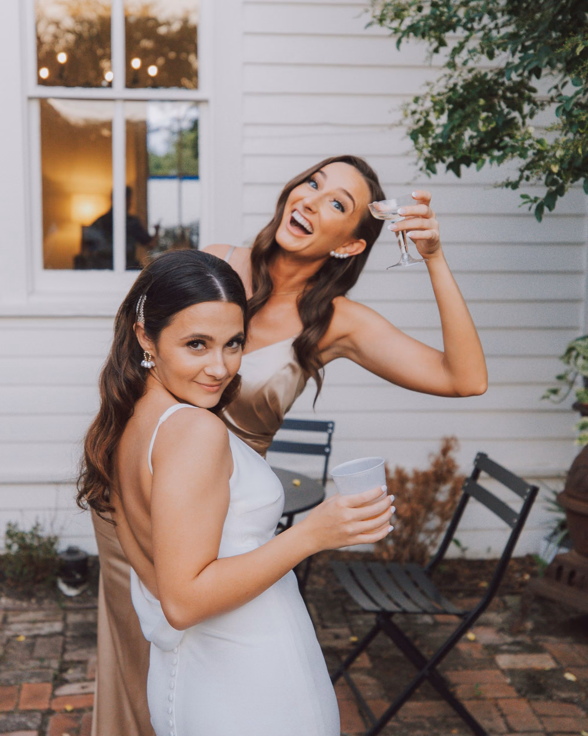 Une bride blanche et son amie dans un chemisier doré partagent un moment joyeux au jardin de leur mariage.