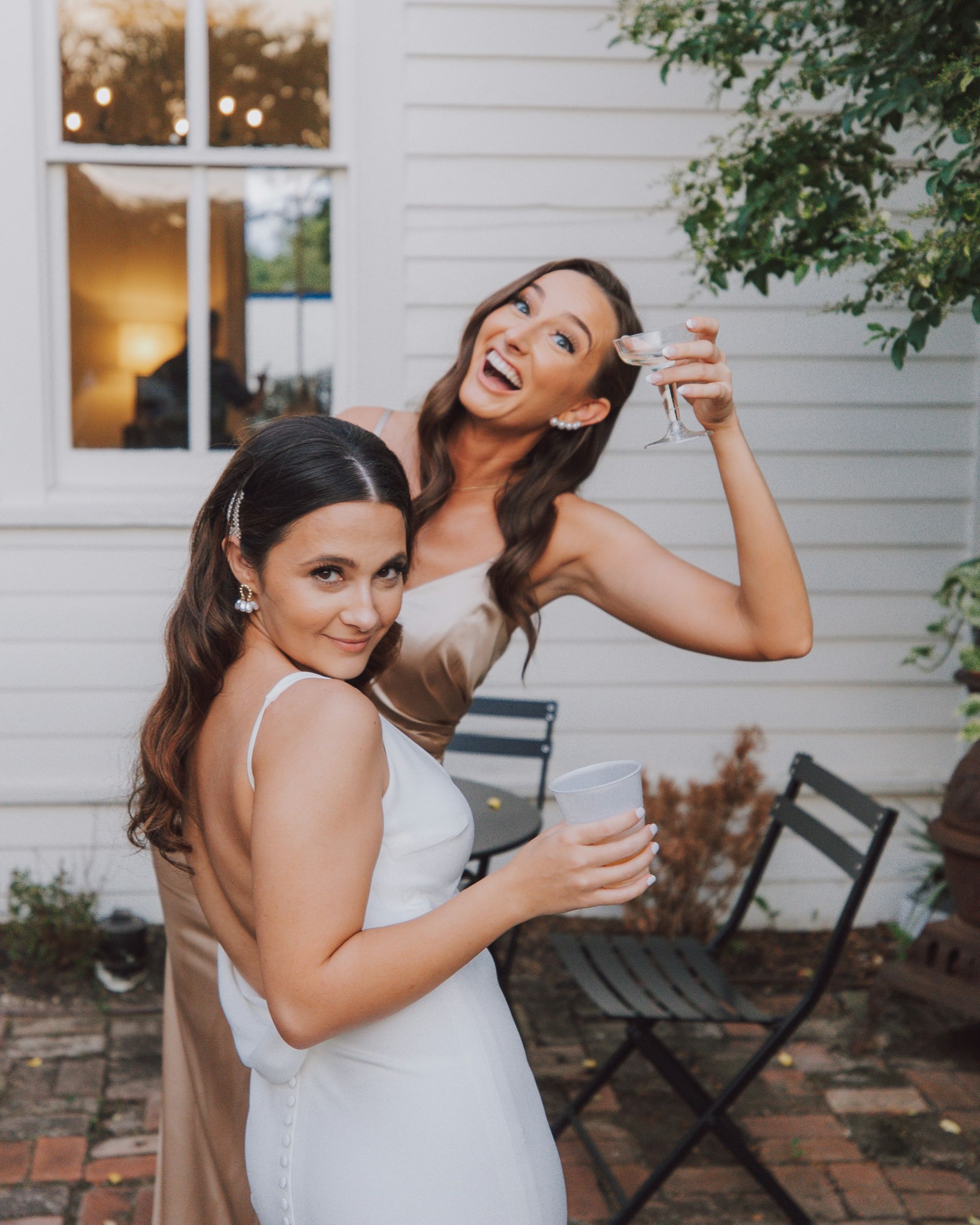 Une bride blanche et son amie dans un chemisier doré partagent un moment joyeux au jardin de leur mariage.