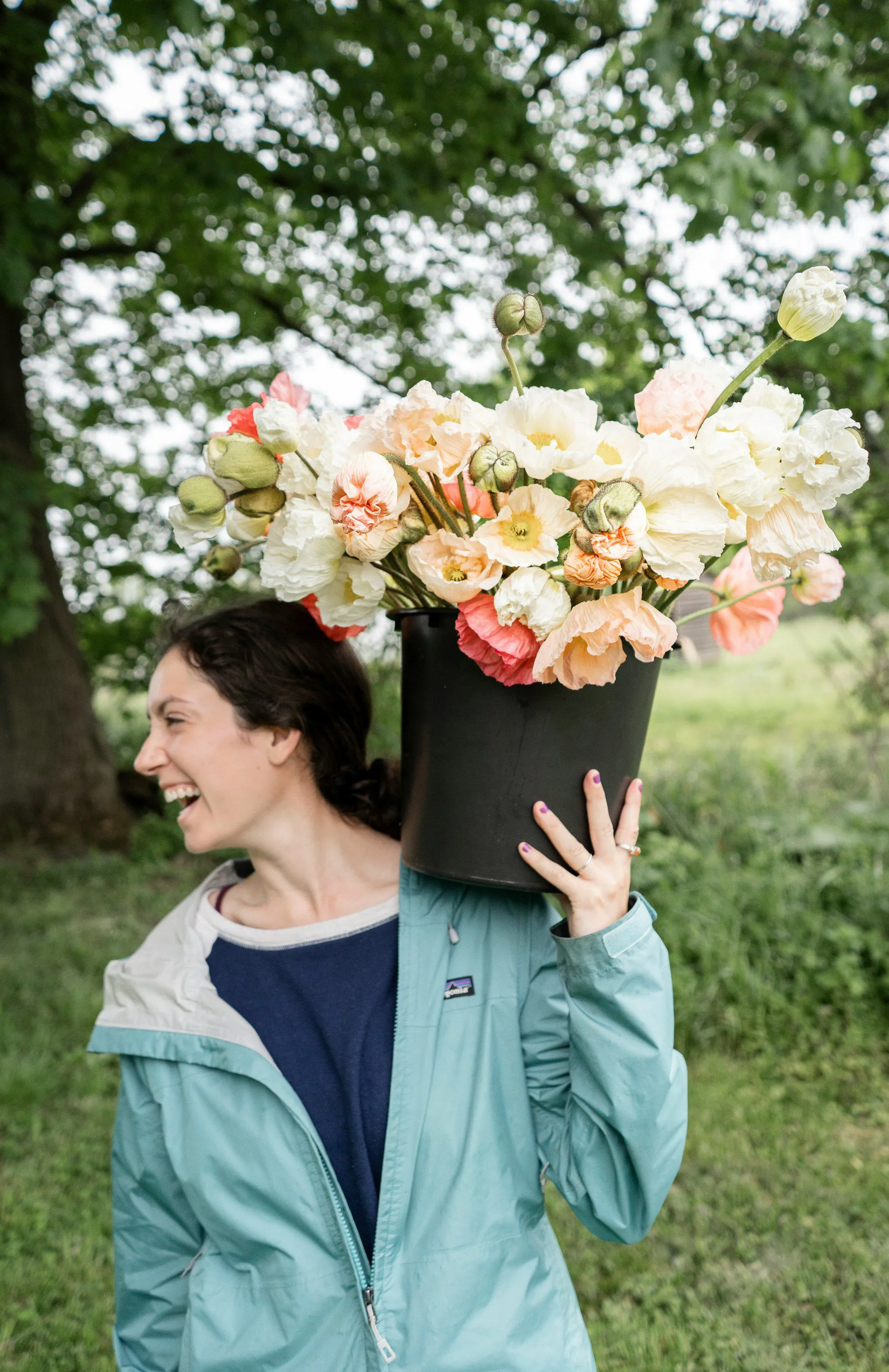 Une femme heureuse porte un grand pot de fleurs dans son dos, renforçant l'ambiance joyeuse et naturelle.