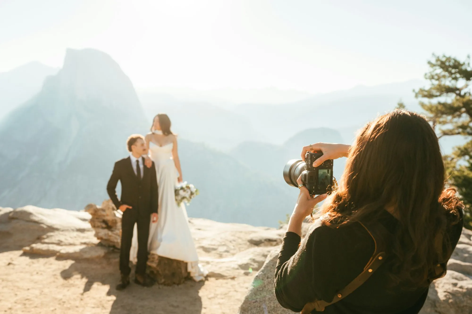 Un couple de mariés pose contre un fond époustouflant de montagnes ensoleillées, capturés par une photographe passionnée.