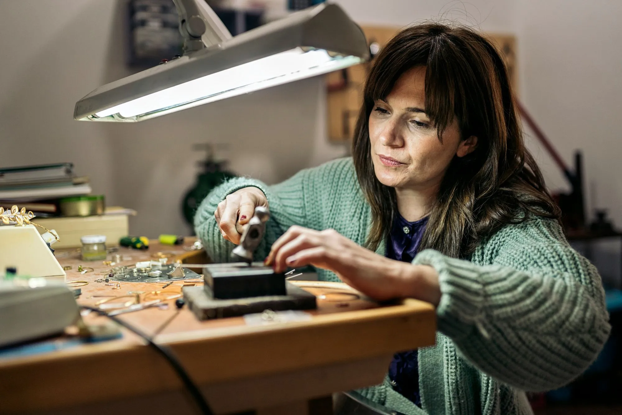 Une femme soigneusement travaillant sur un projet de bijouterie dans un atelier bien éclairé, mettant en valeur la
