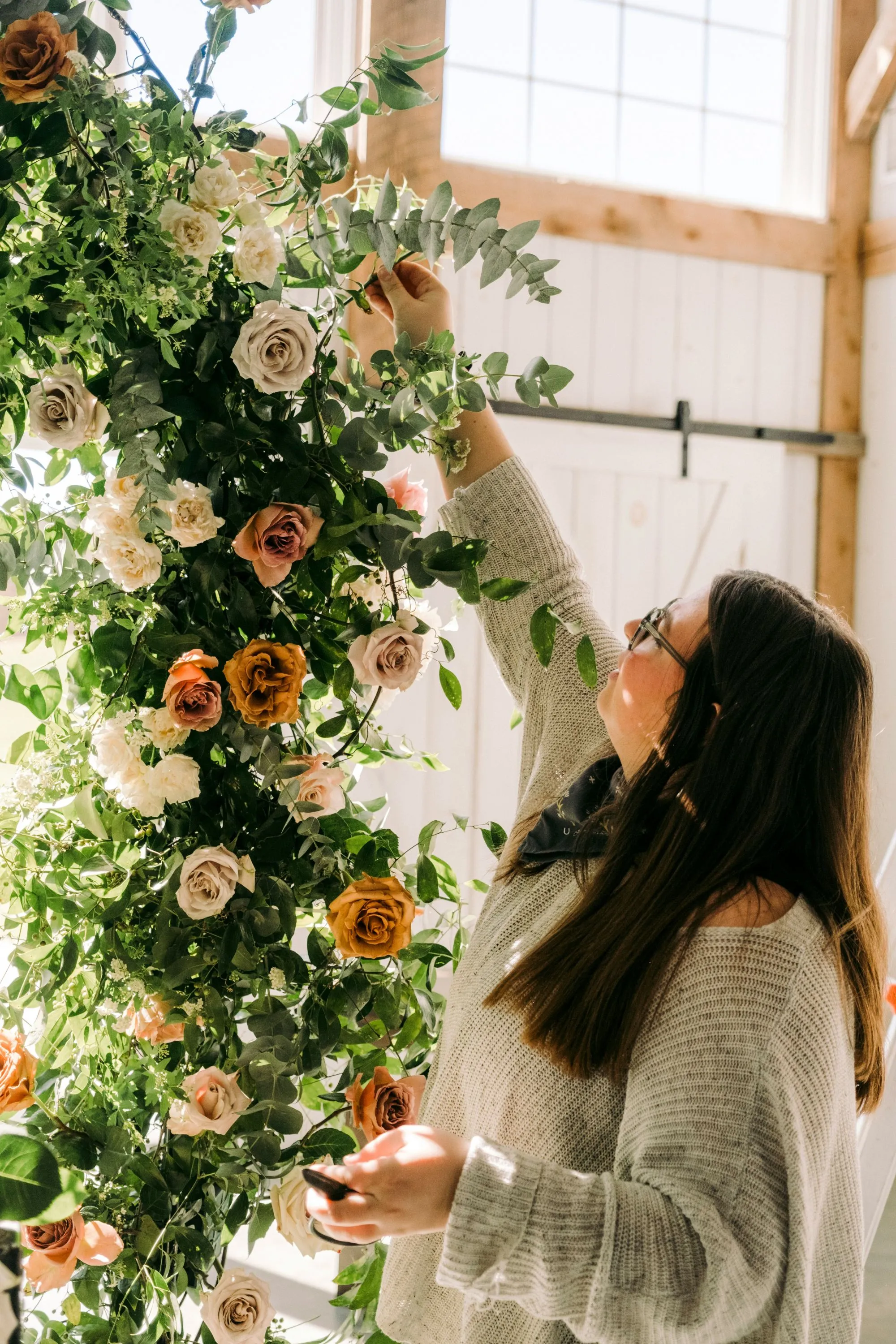 Une jeune femme décore une installation florale luxuriante avec des roses et des feuilles vertes, créant un atmosphère