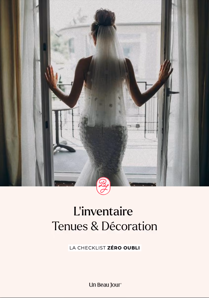 Une mariée dans un vêtement de mariage blanc et orné d'un manteau de dentelle regarde à travers une fenêtre.