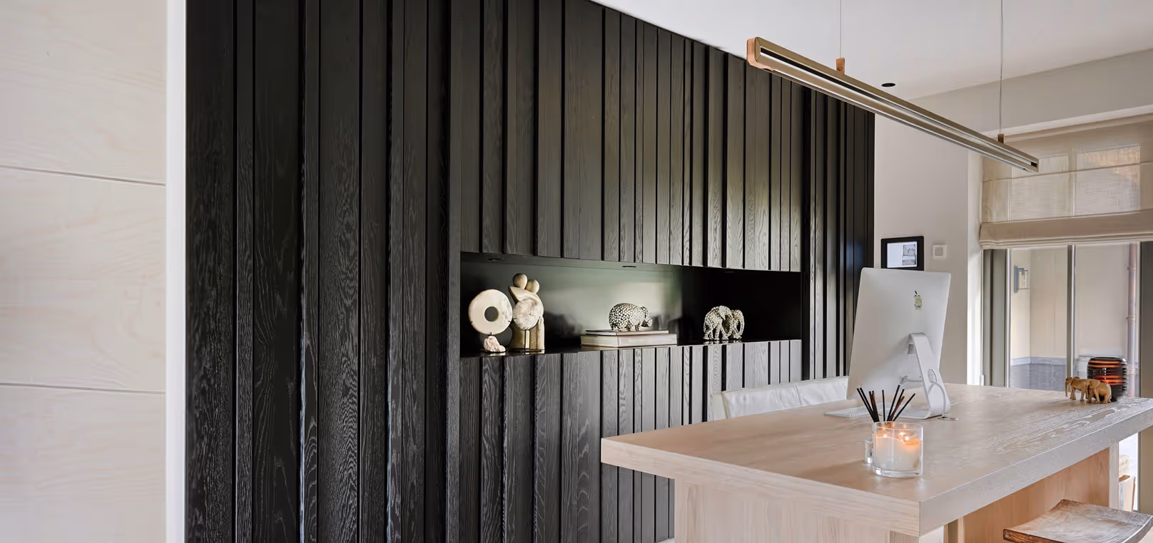 Moderne werkkamer met zwart houten wand, houten bureau, computer en accessoires.