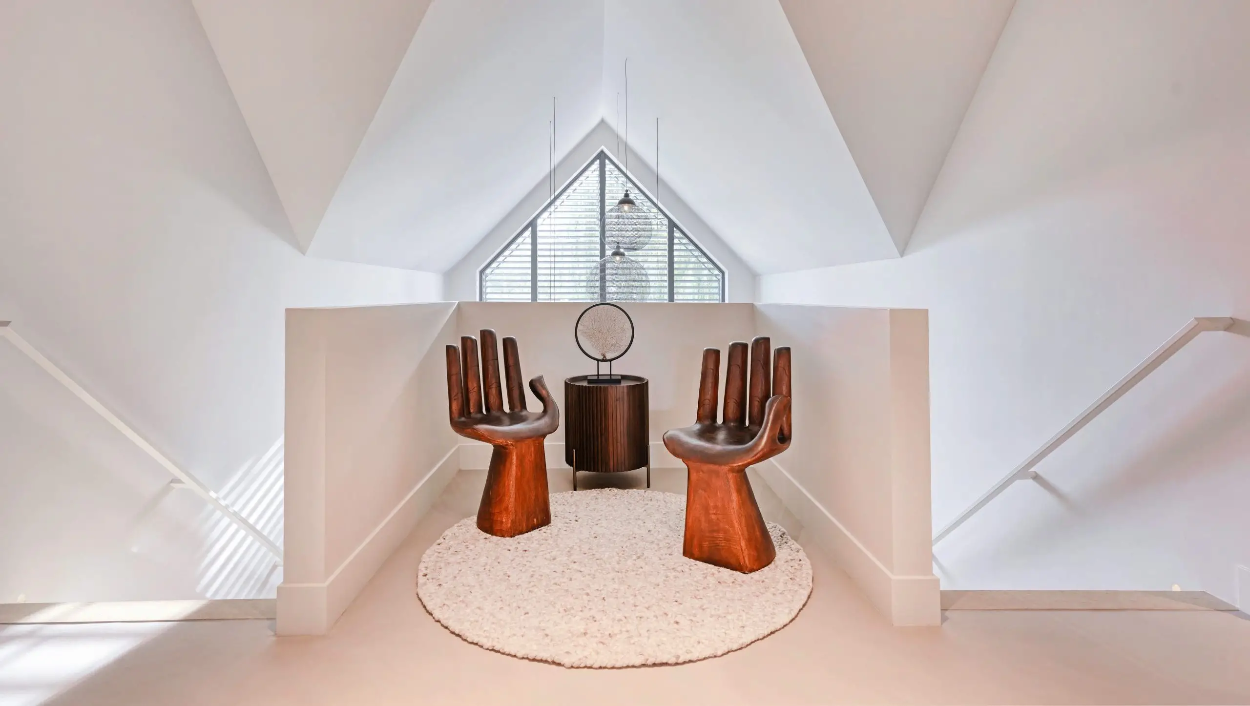 Twee houten handvormige stoelen rondom een rond vloerkleed bij een houten bijzettafel onder een raam.
