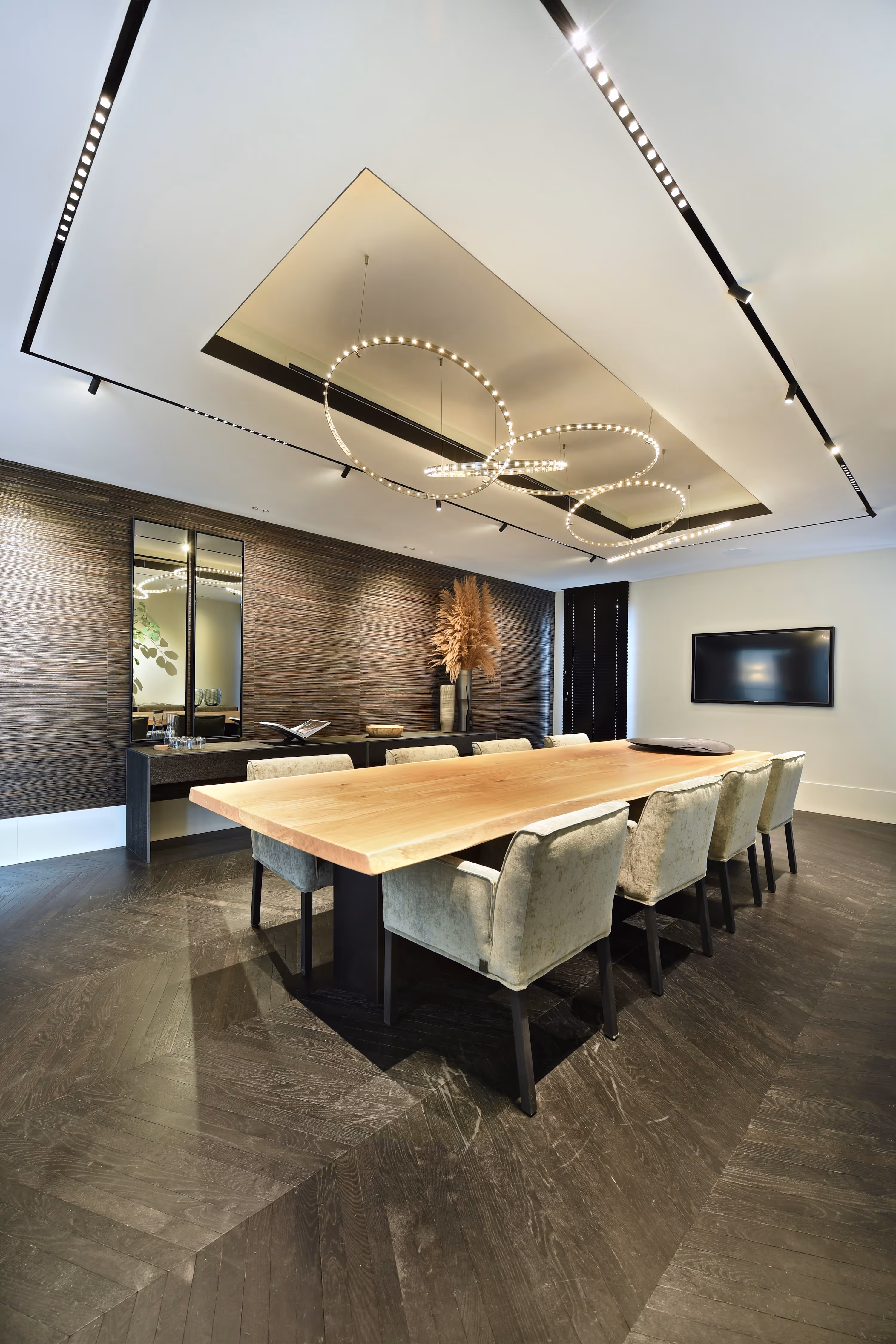 Moderne vergaderruimte met een lange houten tafel, fluwelen stoelen en ronde hanglampen aan het plafond.