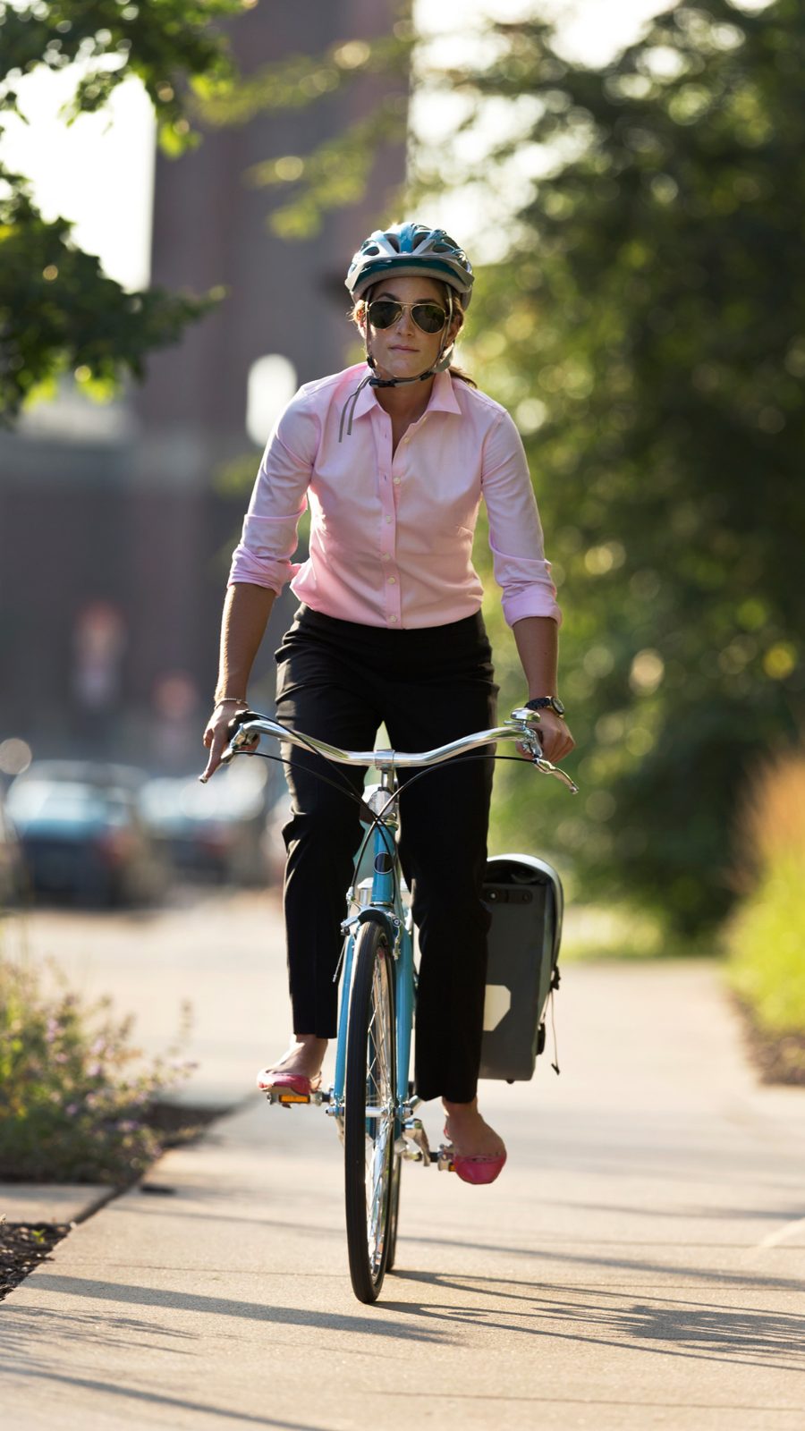 Woman in a pink shirt and helmet riding a blue bicycle on a sunny pathway.