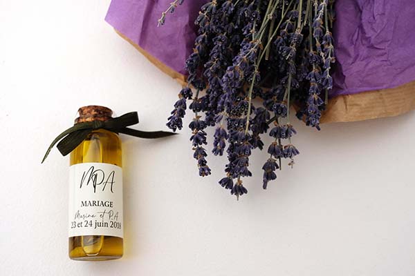 Petite bouteille d'huile d'olive personnalisée et bouquet de lavande séchée sur fond blanc, ambiance bohème.