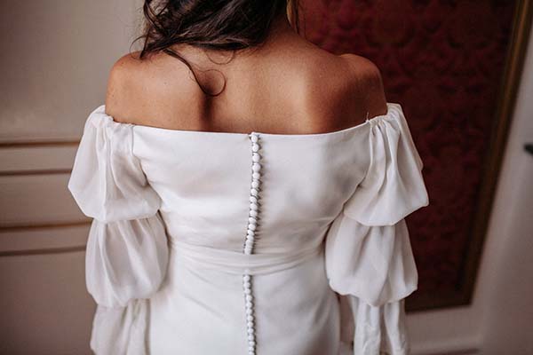 Dos d'une mariée en robe blanche bohème à épaules dénudées et manches bouffantes, fermée par des boutons nacrés.