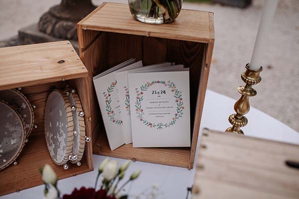 Faire-part botaniques et tambourins dans des caisses en bois clair pour un mariage bohème et naturel.
