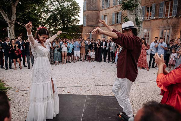Jeunes mariés dansant avec passion lors d'une réception bohème en extérieur, entourés de leurs invités.