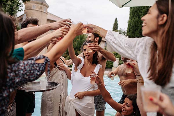 Groupe d'amis souriants trinquant avec des cocktails lors d'une fête estivale en extérieur près d'une piscine.