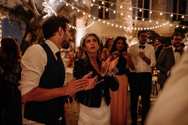 Jeunes mariés et invités festoyant en soirée sous des guirlandes lumineuses lors d'un mariage bohème et chaleureux.