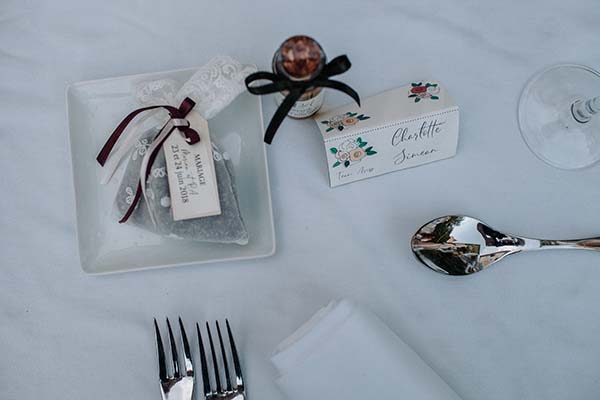 Cadeaux d'invités et couverts sur une nappe blanche pour un mariage bohème, avec détails floraux et dentelle.