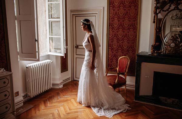 Mariée de profil en robe blanche et voile long dans un salon classique aux tons chauds et boiseries.