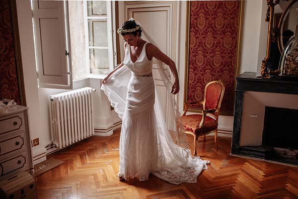 Mariée en robe blanche ajustée et voile, posant dans un salon classique au parquet en chevrons.