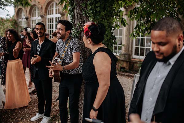 Des invités élégants et un musicien à la guitare animent un cocktail en extérieur dans une ambiance festive et bohème.