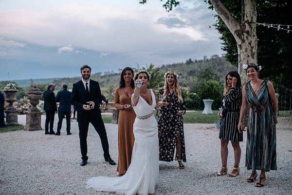 Une mariée en robe blanche et ses invités rient ensemble lors d'une réception bohème en extérieur au crépuscule.