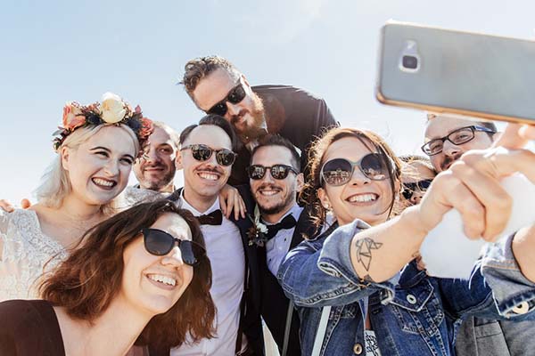 Un groupe d'invités souriants et lookés rock prennent un selfie joyeux lors d'un mariage en plein air.