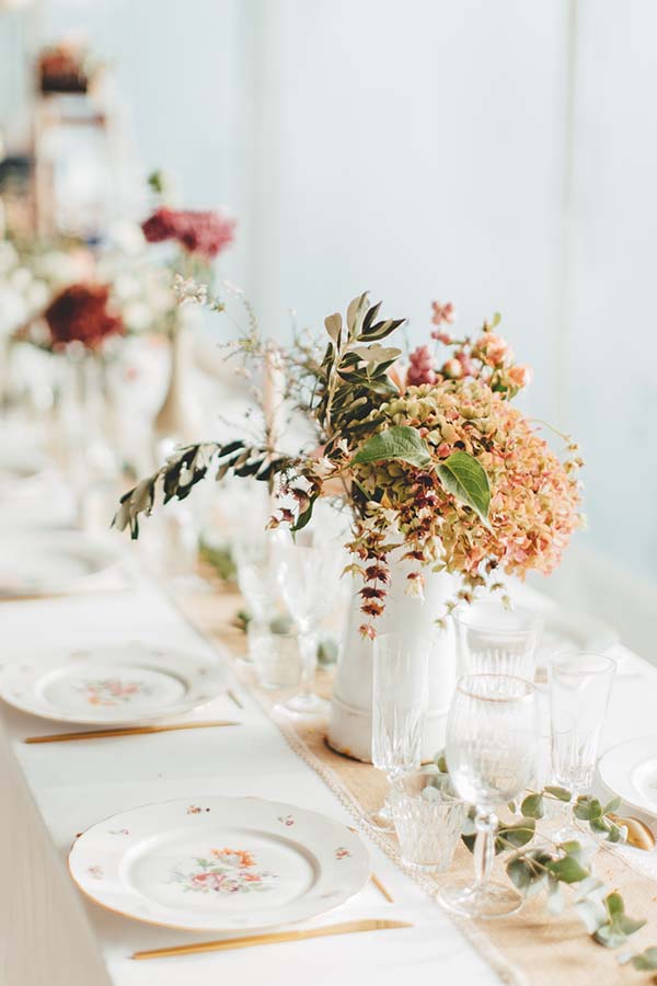 Décoration de table champêtre avec un bouquet floral aux tons chauds et une vaisselle vintage raffinée.