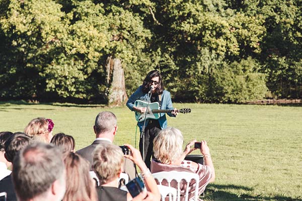 Une musicienne en veste bleue joue de la guitare électrique devant des invités lors d'un mariage en plein air.