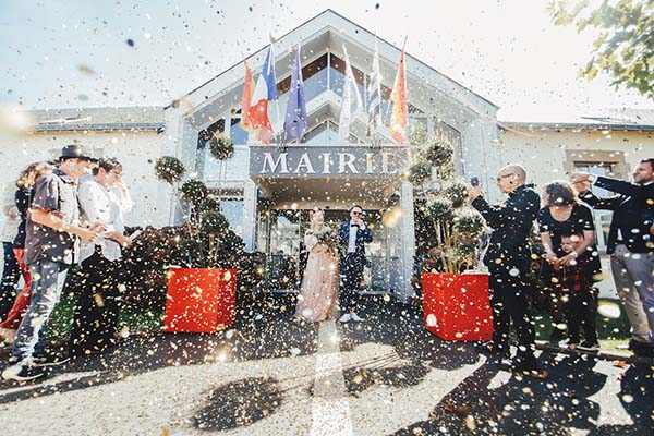 Jeunes mariés sortant de la mairie sous une pluie de confettis dorés, entourés d'invités dans une ambiance festive.