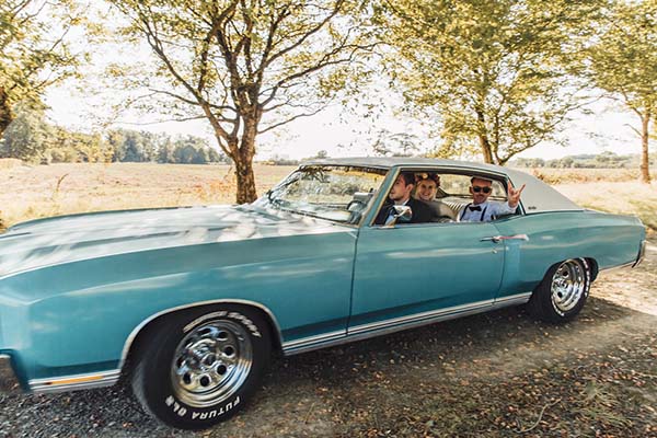 Couple souriant dans une voiture ancienne bleue ciel, ambiance rock et champêtre en plein air.
