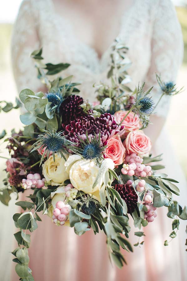 Bouquet de mariée champêtre aux tons bordeaux, rose et crème avec eucalyptus et chardons bleus.