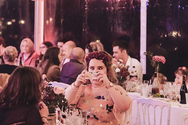 Une invitée à une couronne de fleurs s'amuse avec des accessoires lors d'une réception de mariage à l'ambiance festive.
