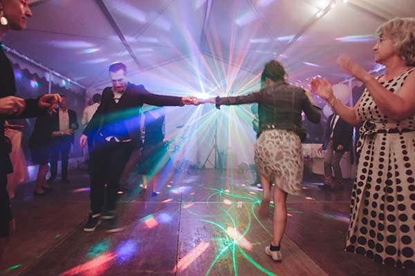 Jeunes mariés dansant sous des jeux de lumières colorés lors d'une soirée de mariage festive et dynamique.