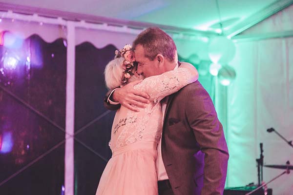 Un couple de mariés s'enlace tendrement sous des lumières roses et vertes lors de leur réception.