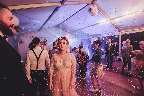 Mariés et invités festoyant sous un chapiteau avec des confettis, dans une ambiance rock et chaleureuse.