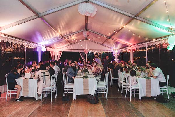 Dîner de mariage convivial sous un chapiteau illuminé, avec des invités élégants autour de tables blanches.