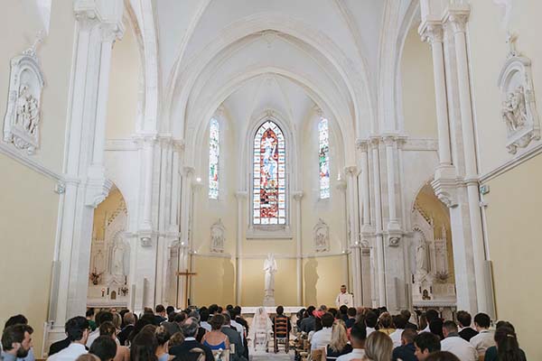 Intérieur d'une église lumineuse et blanche où des invités assistent à une cérémonie de mariage.