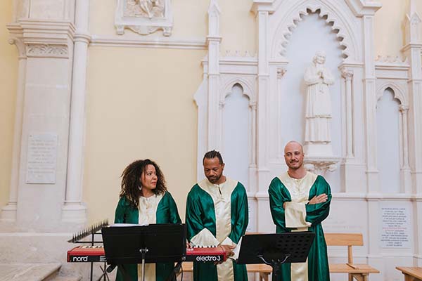 Trois chanteurs en robes vertes et blanches se produisent devant un clavier dans une église lumineuse.