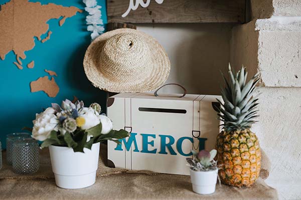 Décoration bohème avec fleurs blanches, ananas, chapeau de paille et boîte Merci sur un fond bleu turquoise.