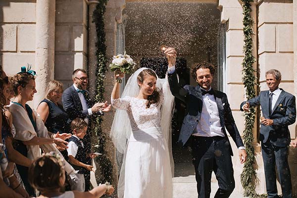 Jeunes mariés rayonnants sortant d'une église sous une pluie de confettis, entourés de leurs invités.