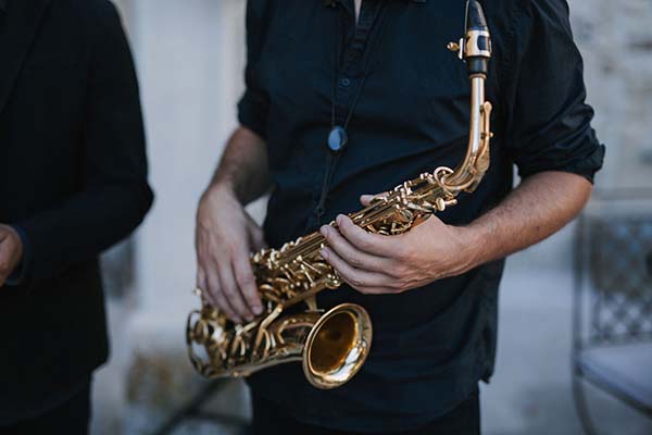 Gros plan d'un musicien en chemise noire tenant un saxophone doré lors d'un mariage élégant et décontracté.