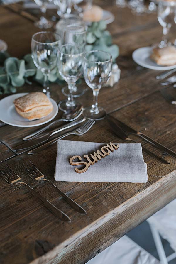 Détail d'une table de mariage rustique en bois avec un marque-place personnalisé au nom de Simon et un petit pain.