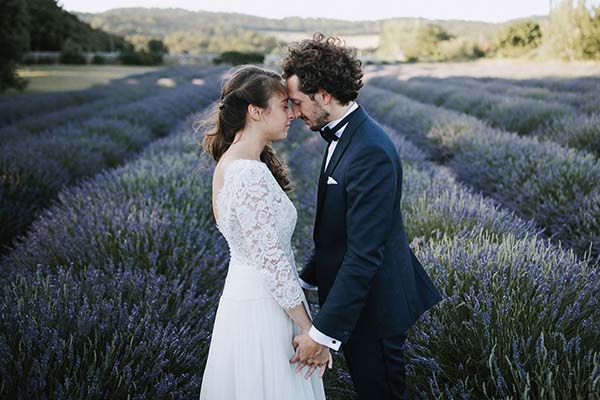 Jeunes mariés s'embrassant tendrement au milieu d'un champ de lavande violette sous une lumière douce.