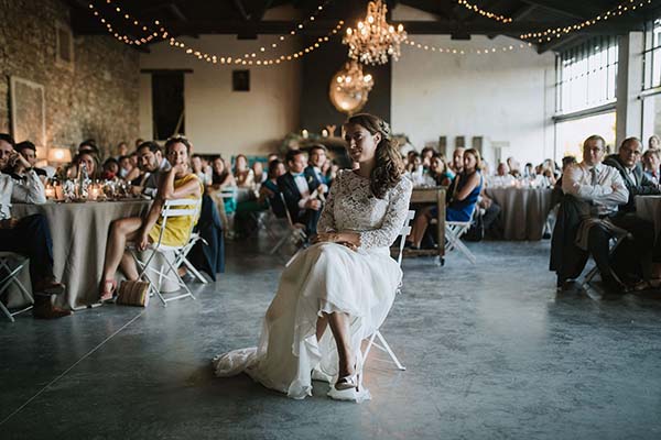 Une mariée en robe blanche assise au centre d'une salle festive et lumineuse entourée de ses invités.
