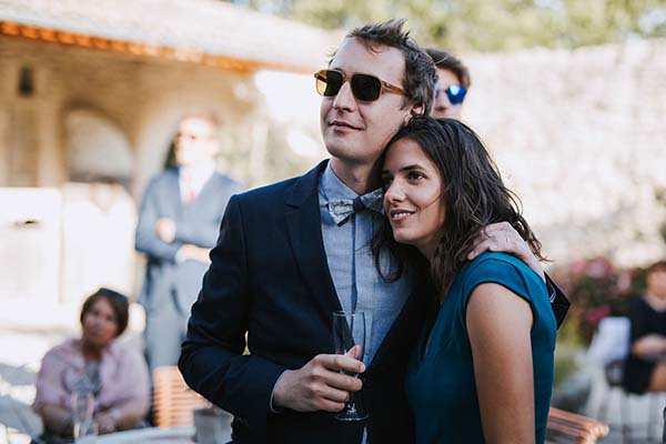 Couple élégant et complice, l'homme en costume bleu et la femme en robe turquoise, lors d'un mariage décontracté.