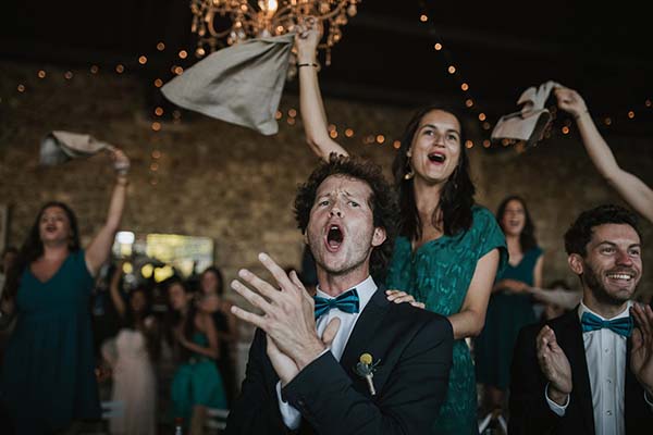 Invités joyeux en tenues bleu canard et costumes célébrant avec enthousiasme lors d'une soirée de mariage festive.