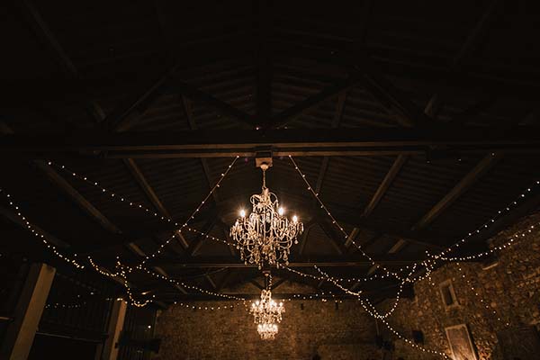 Lustres et guirlandes lumineuses illuminent l'intérieur chaleureux d'une grange en pierre pour un mariage intimiste.