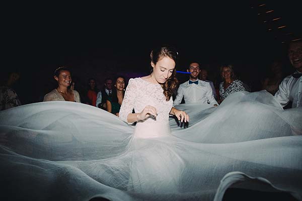 Mariée en robe blanche tournoyant avec joie lors de sa soirée de mariage, entourée de ses invités.